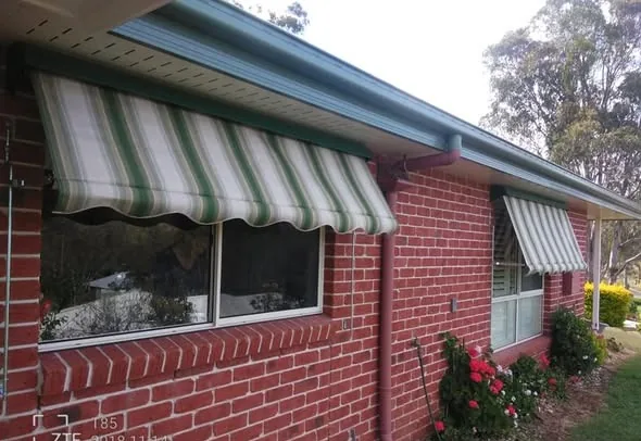 Green and cream striped window awnings on a brick home