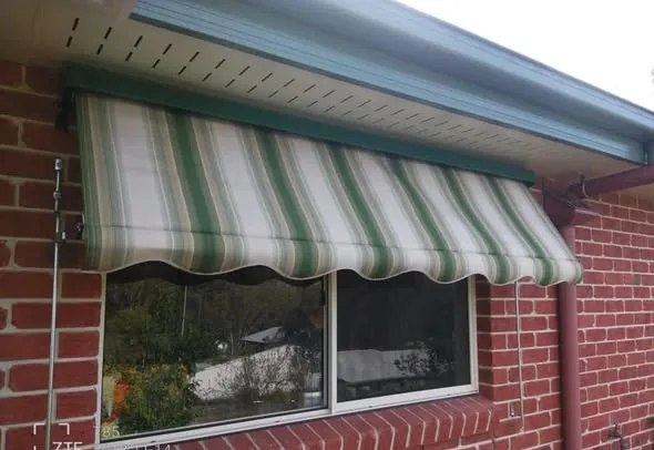 Green striped window awning over a brick home window